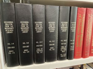 26 thick black bound volumes of the Occasional Bulletin from the Missionary Research Library on a bookshelf